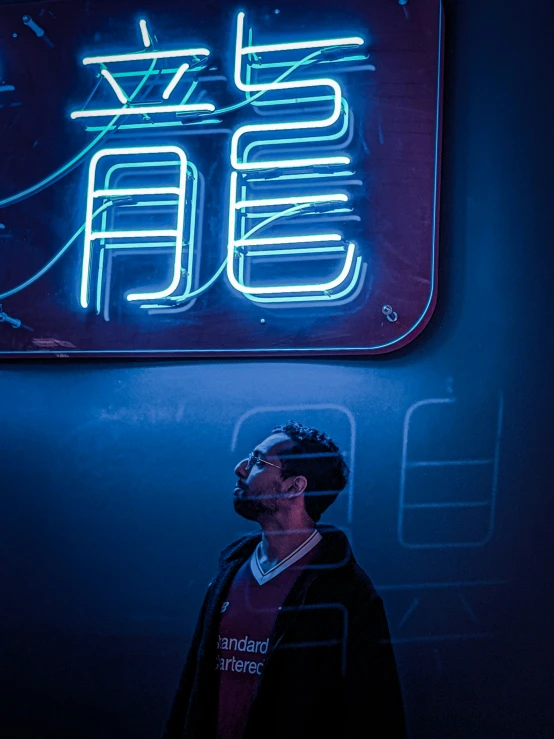 a young man standing in front of a neon sign