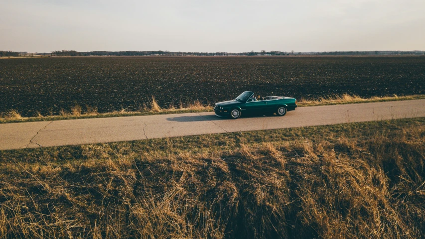 a green sports car parked by a road and a field