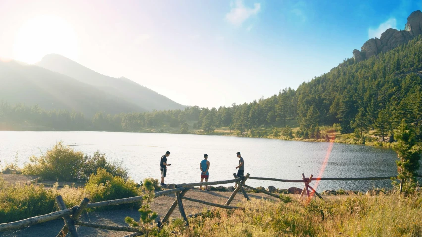 four men standing on top of a wooden railing near a lake