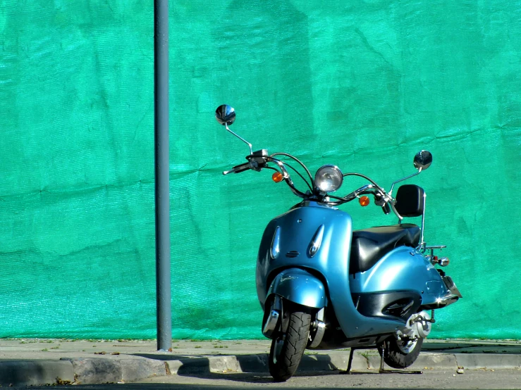 the motorcycle is parked on the sidewalk near a green wall