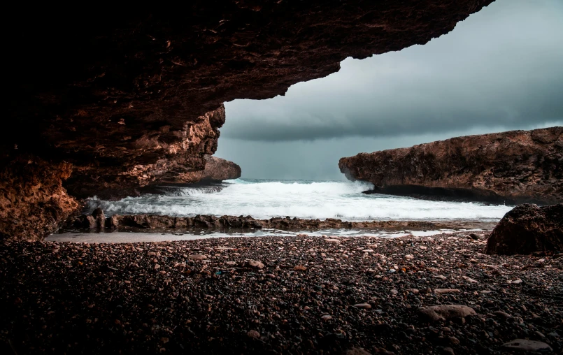 view of beach from inside of cave, under stormy skies