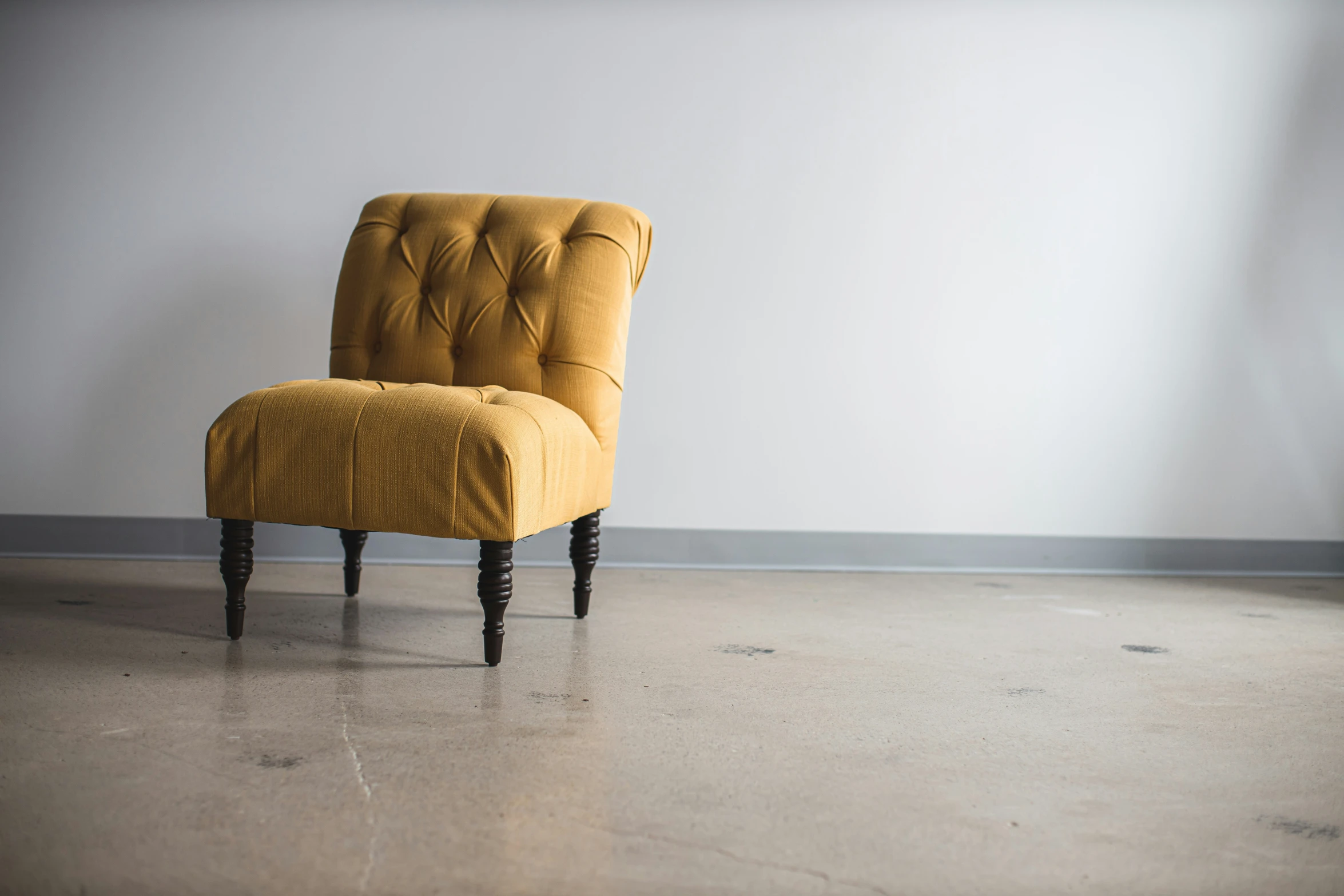 a small yellow chair with wooden legs sits against a white wall