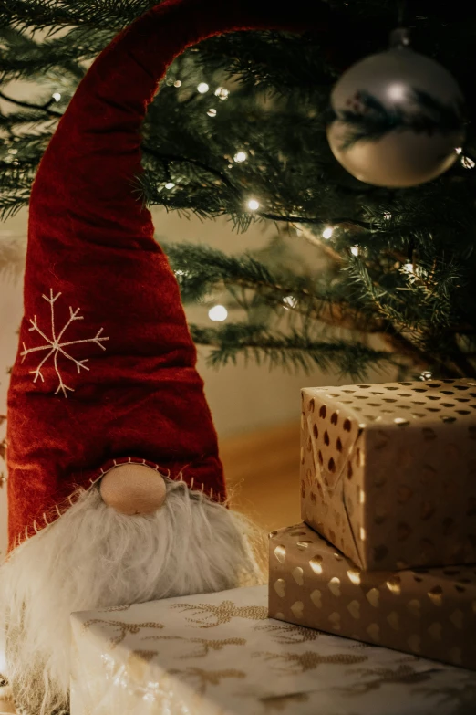 a small gnome is standing near some presents under a christmas tree