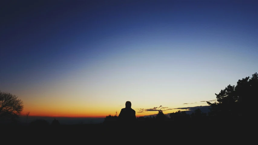 a woman sits in the distance while looking at the sun