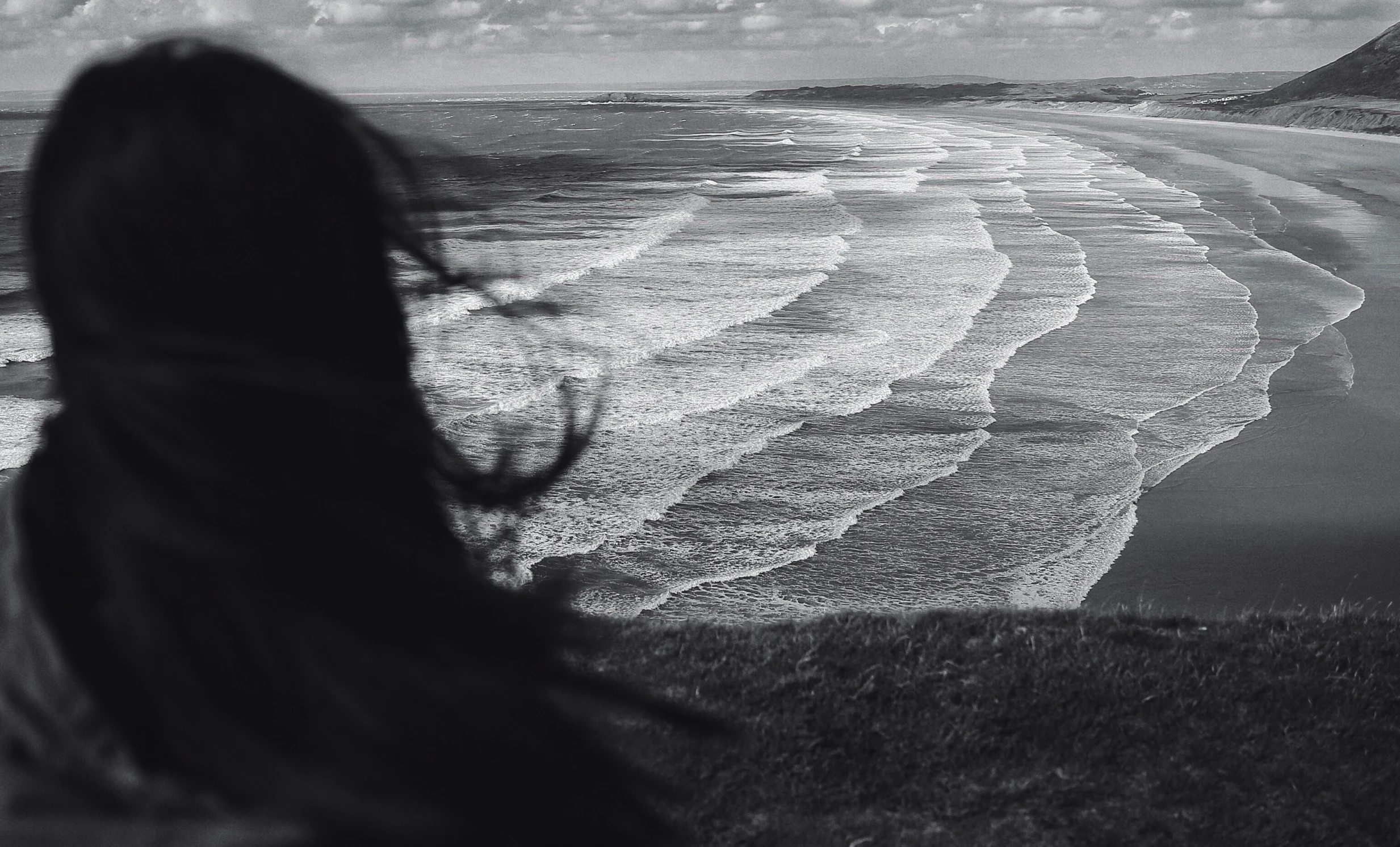 the silhouette of a woman against an overcast sky on the shore of a rocky beach