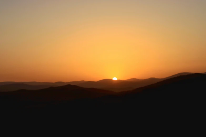 the sun is setting over mountains with the silhouettes of a horse