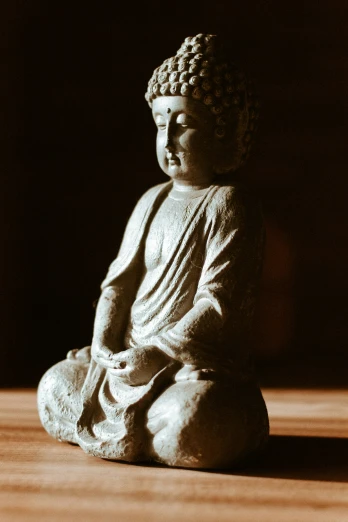 buddha statue sitting on wood floor next to dark wall