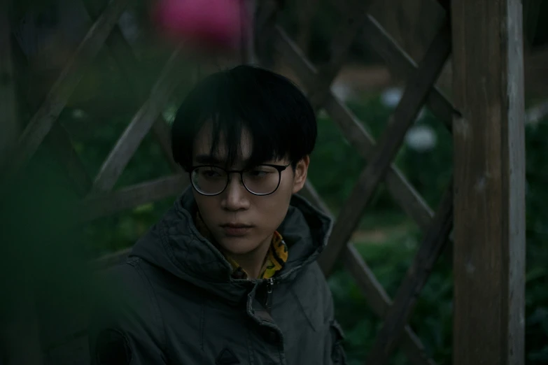 a man in glasses stares out from behind a fence