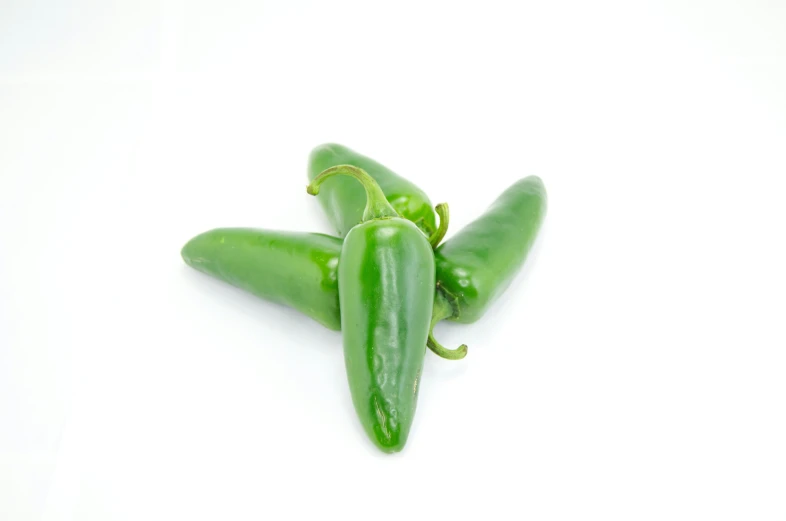 three green peppers are piled together on a white surface