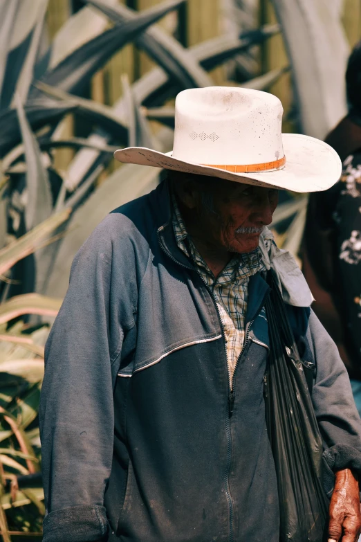 a man with a cowboy hat standing in front of a plant