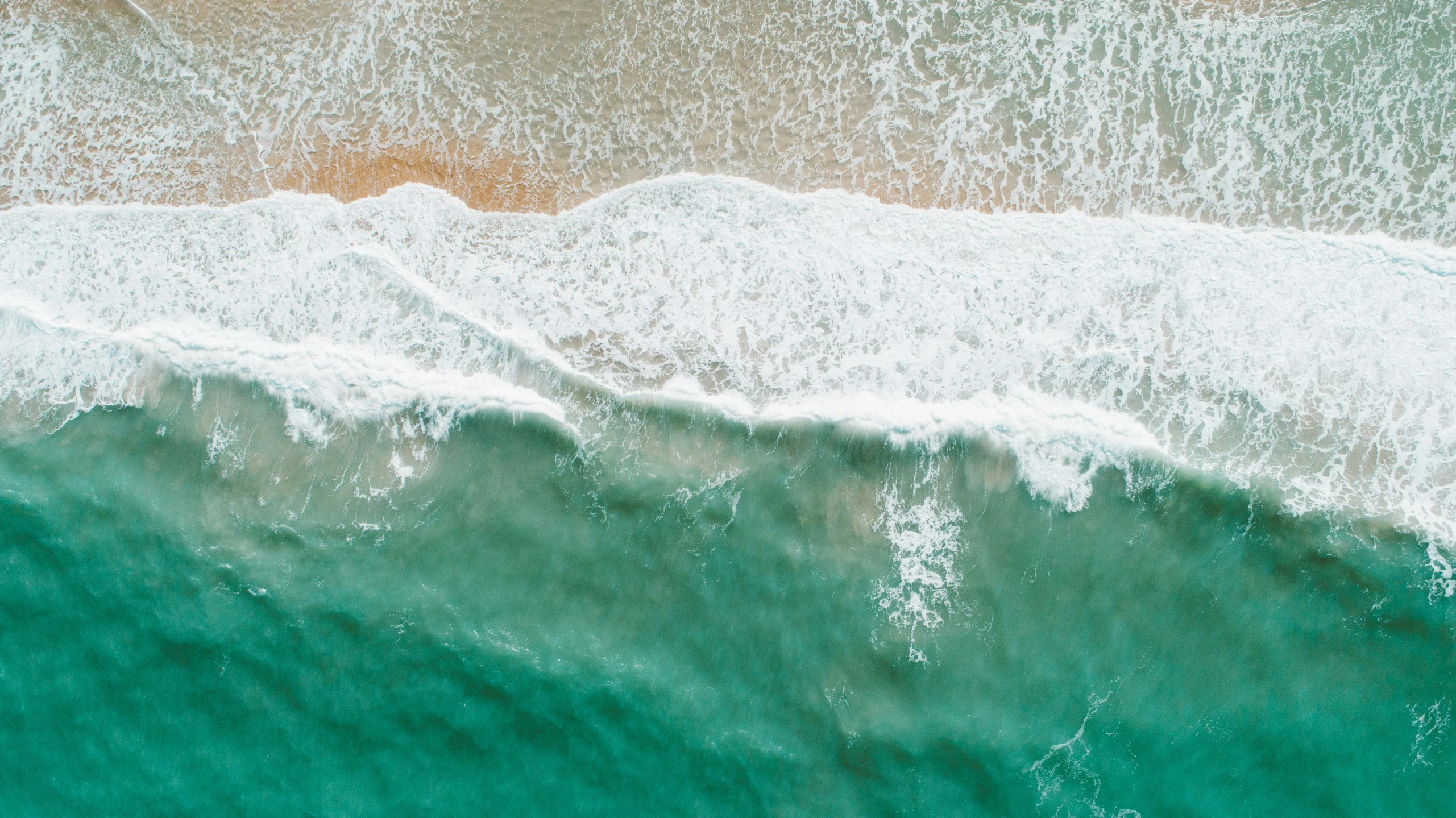 an aerial view of the ocean water and sand