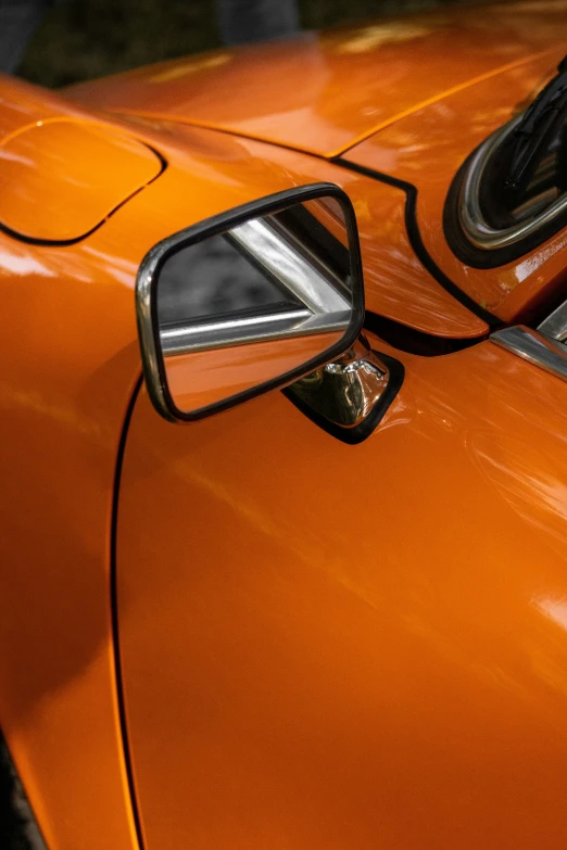 the reflection of an orange classic car in a rear view mirror