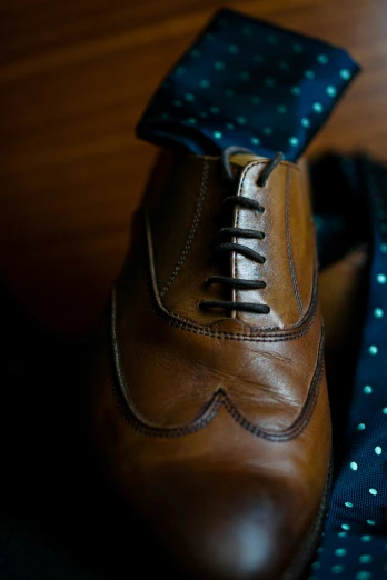 a tie and brown leather dress shoe on a wooden table
