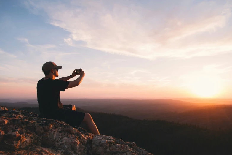 a man sitting on top of a rock hill taking a picture