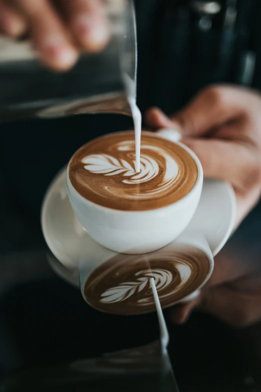 someone pouring cream onto a cappuccino made from an espresso machine