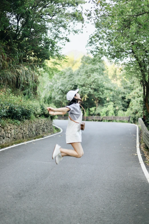 a woman in a white dress is jumping while on a road