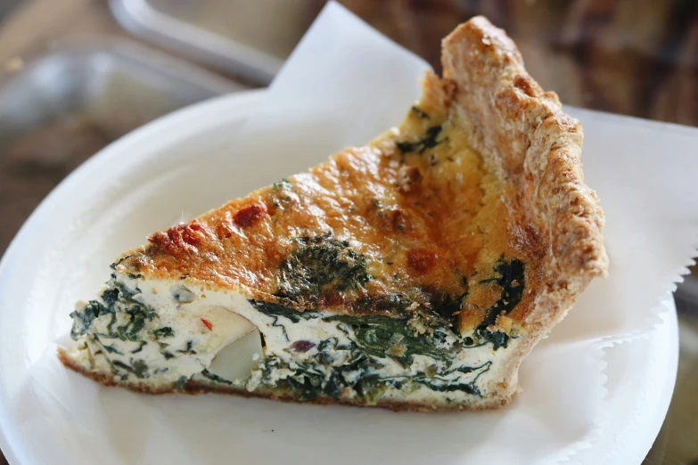 a slice of quiche on a paper plate