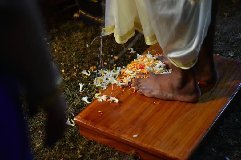 a barefoot person stepping on a wooden plank with flower petals