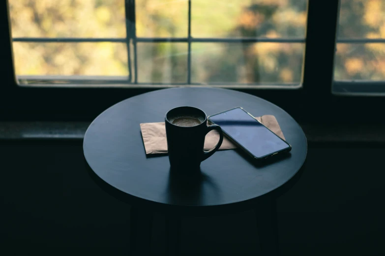 the table has two cell phones, a notebook and a cup on it