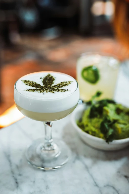 two cocktails sit on a table next to green and white vegetables