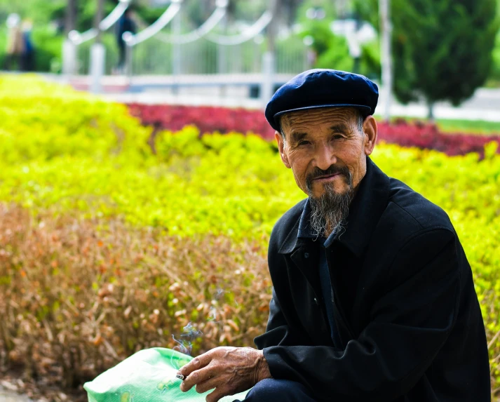 man with beard and hat sitting in the park near flowers