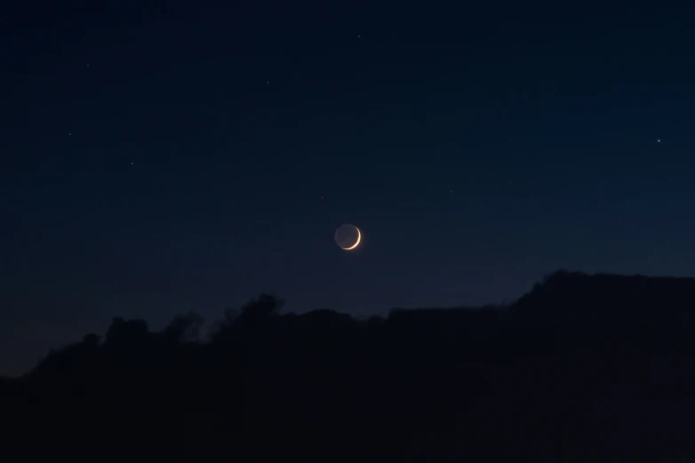 the moon is rising behind a hill at night