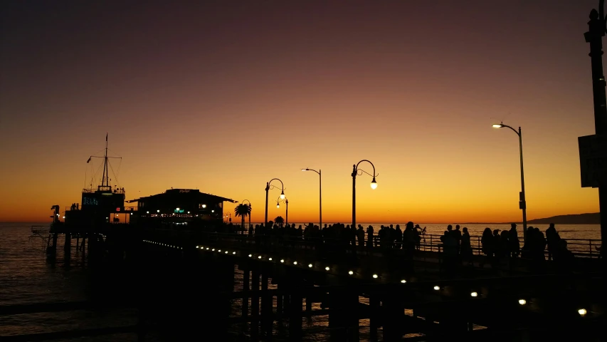 the sun sets over a pier with people