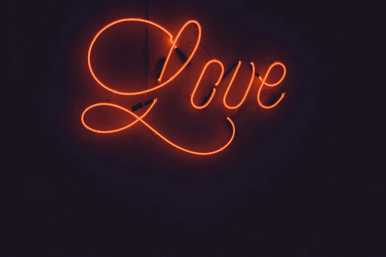 an orange neon love sign hangs from a dark background