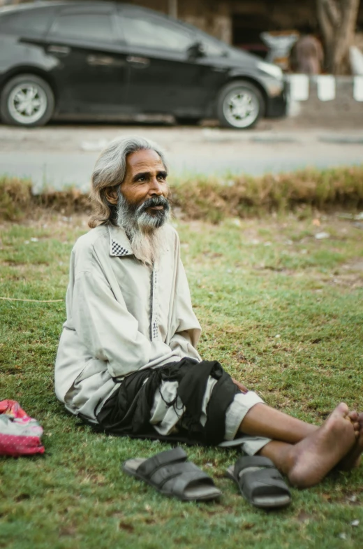 an elderly man sitting on the ground in a grassy area