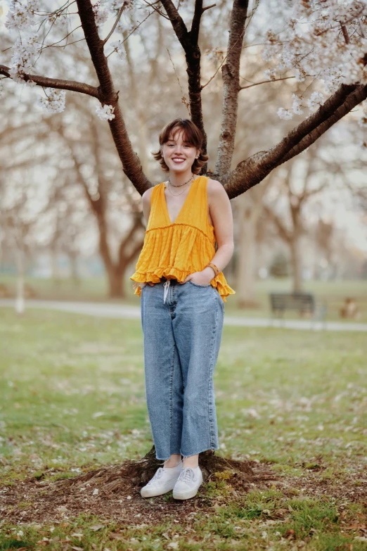 a woman in high waist jeans poses under the blossomy tree