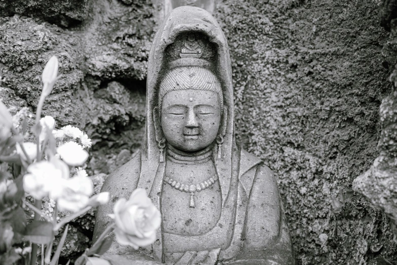 buddha statue sitting next to flowers in black and white