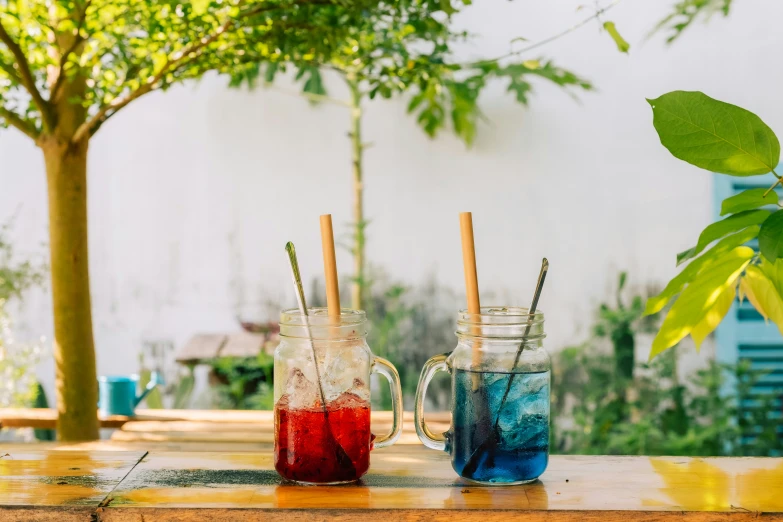 two glasses with colorful drinks sitting on a table