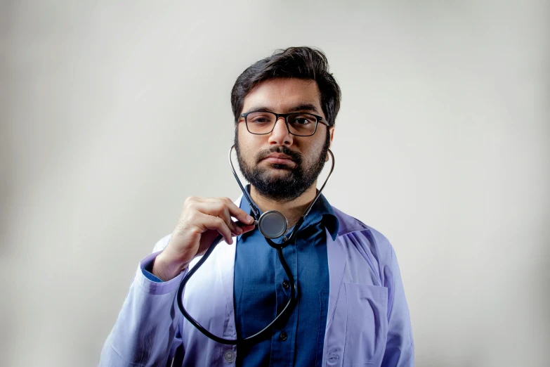 a man with glasses holding a stethoscope to his neck