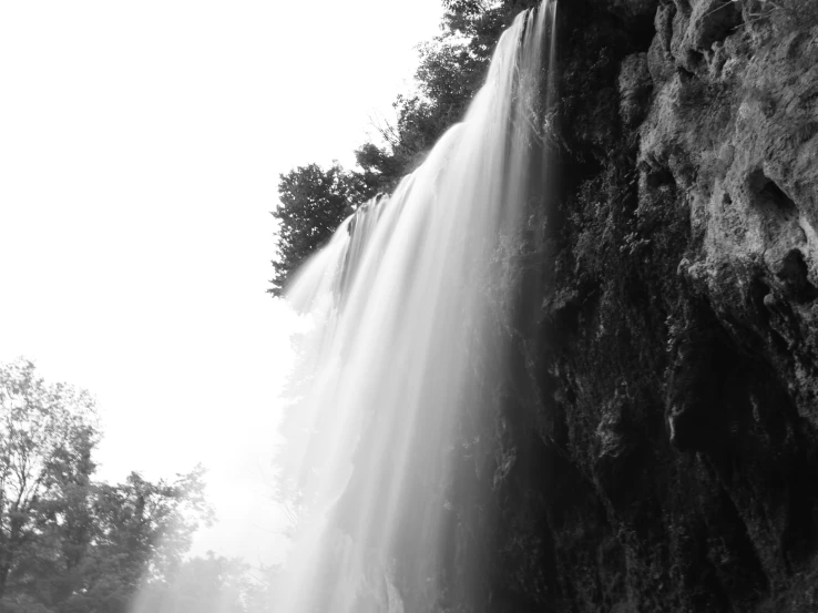 large waterfall in front of wooded cliff and light coming from below