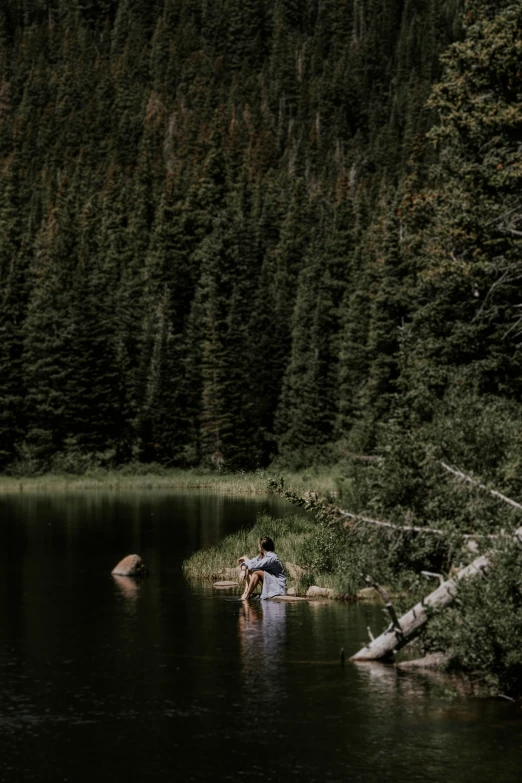a man sitting in the middle of the water next to a forest