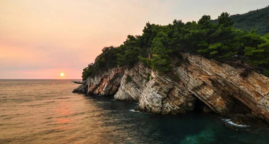 the sun setting over a wooded area near the ocean