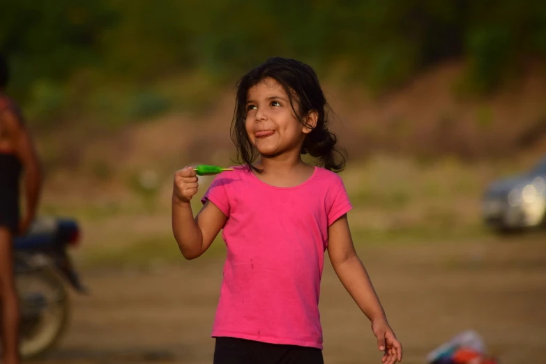  in pink shirt standing on dirt with small green object