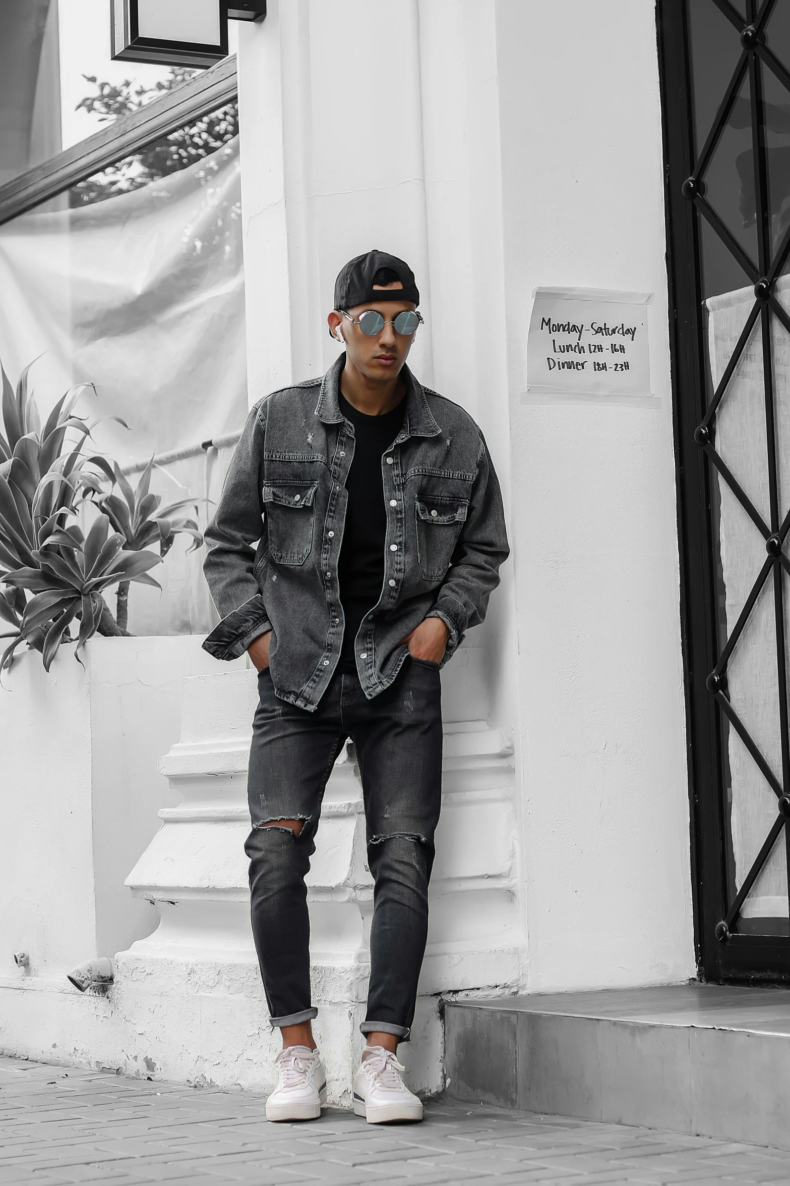 a man standing against a wall wearing ripped jeans