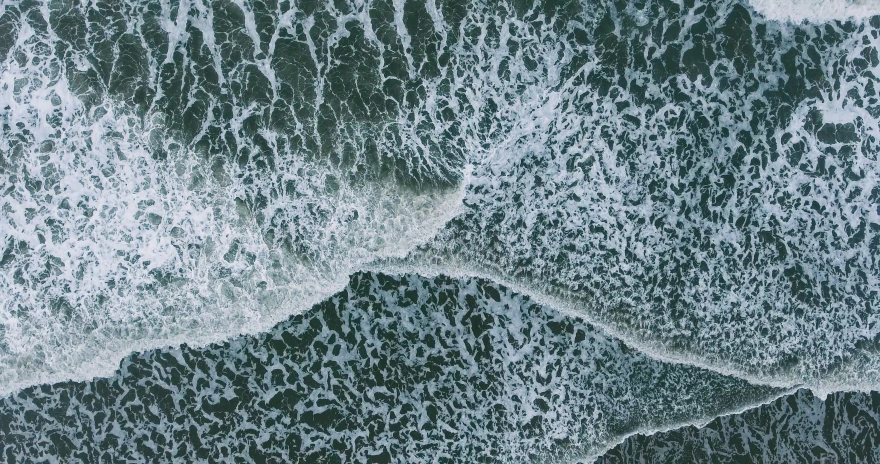 the ocean with waves on it and black sand below