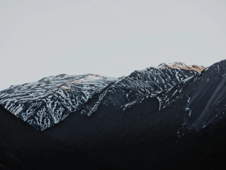 a group of snow covered mountains standing under a gray sky