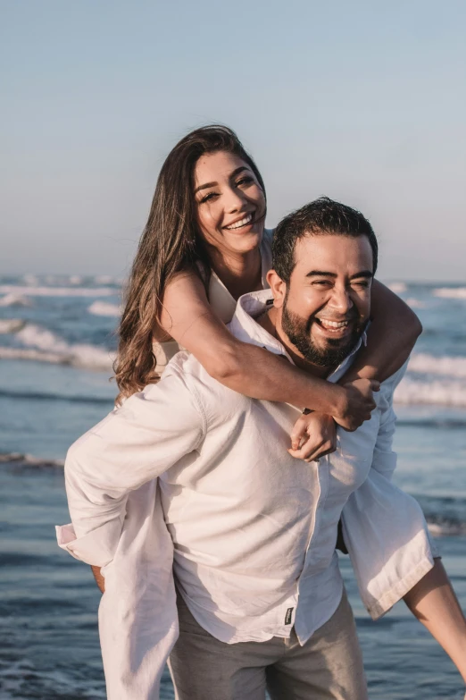 an image of a man giving his girlfriend piggyback her at the beach