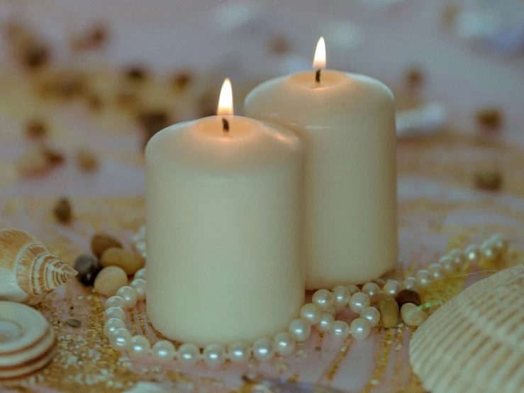 two white candles on top of a table next to shells