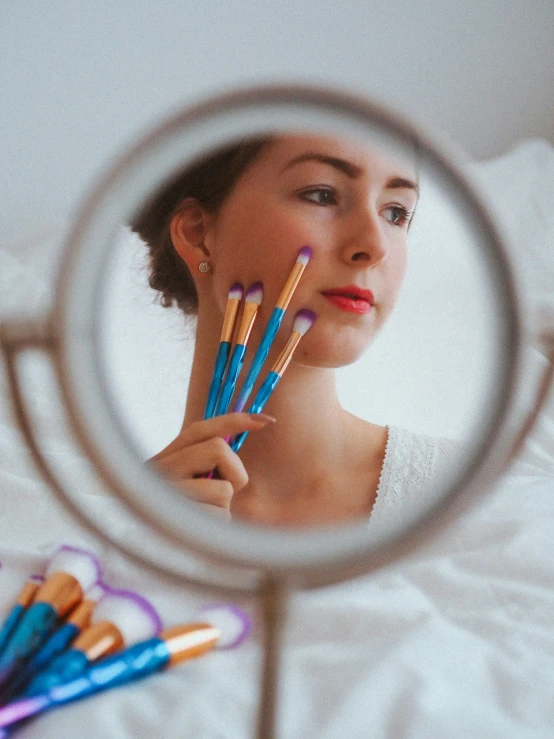 a girl holding up pencils to her face and looking in a mirror