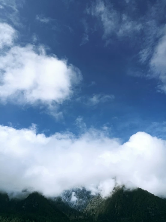 some clouds in the sky over mountains and trees