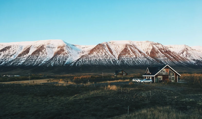 a house and car in a field with snowy mountains in the background