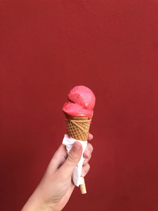 a hand is holding a pink ice cream cone