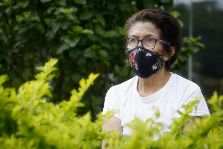 a woman wearing a face mask stands in the bushes