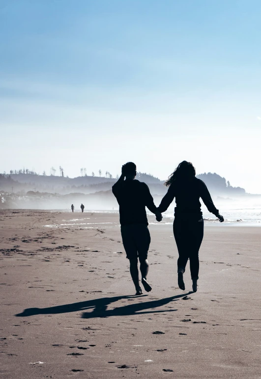 a couple running on the beach with a kite flying above them