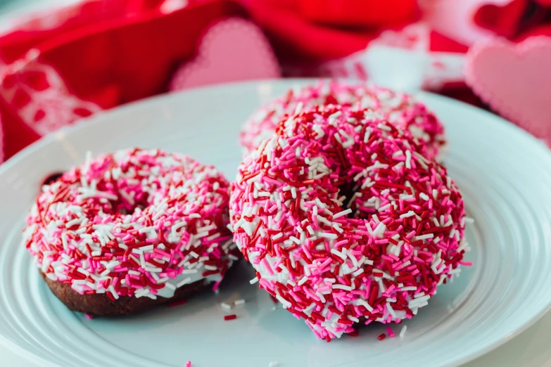 two donuts on a plate with sprinkles and hearts in the background