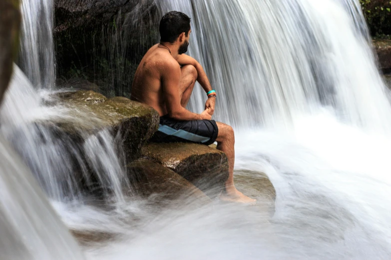 shirtless man sitting at top of waterfall